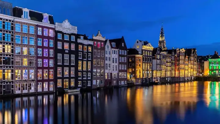 Colorful windows and canal houses at blue hour with water reflection in Damrak Amsterdam Netherlands