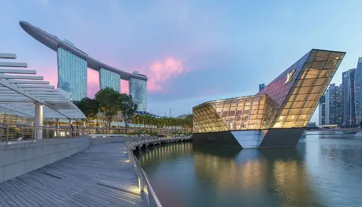 Marina Bay Sands and illuminated polyhedral building Louis Vuitton over the water at blue hour with pink clouds in Singapore